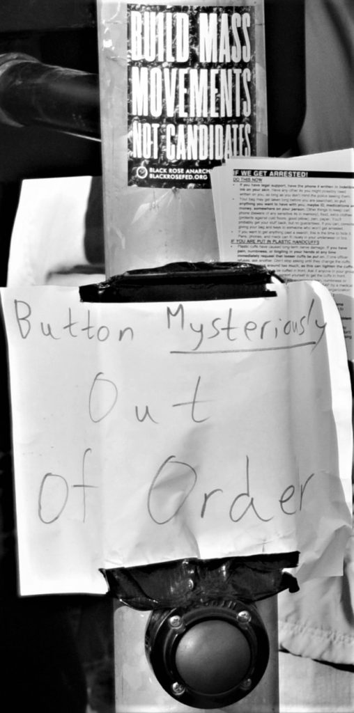Sign on the crosswalk button: "Button mysteriously out of order"